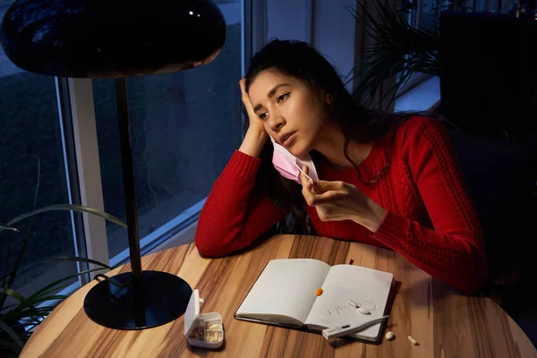 Donna malata con pillole e termometro su un tavolo che lavora su un computer portatile da casa in isolamento di quarantena . — Foto Stock