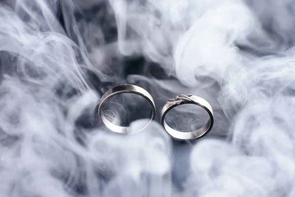 Two golden wedding rings with white smoke around, copy space and black background — Stock Photo, Image