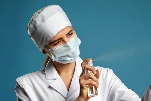 Jovem médica usando spray anti-séptico spray sobre fundo azul — Fotografia de Stock