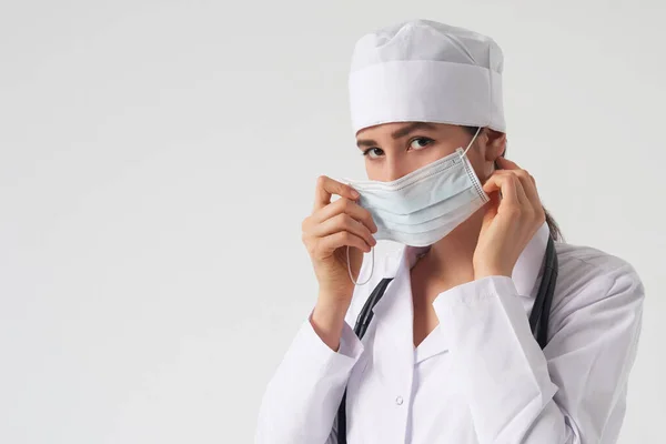 Портрет молодой женщины-врача, надевающей защитную медицинскую маску на белом фоне, копировальное пространство — стоковое фото
