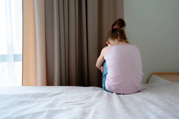 Küçük üzgün bir kız yatak odasında, arka planda oturuyor. — Stok fotoğraf