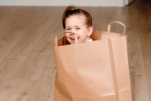 Liten flicka sitter i Brown papper shoppingväska, leka barn koncept med kopieringsutrymme — Stockfoto