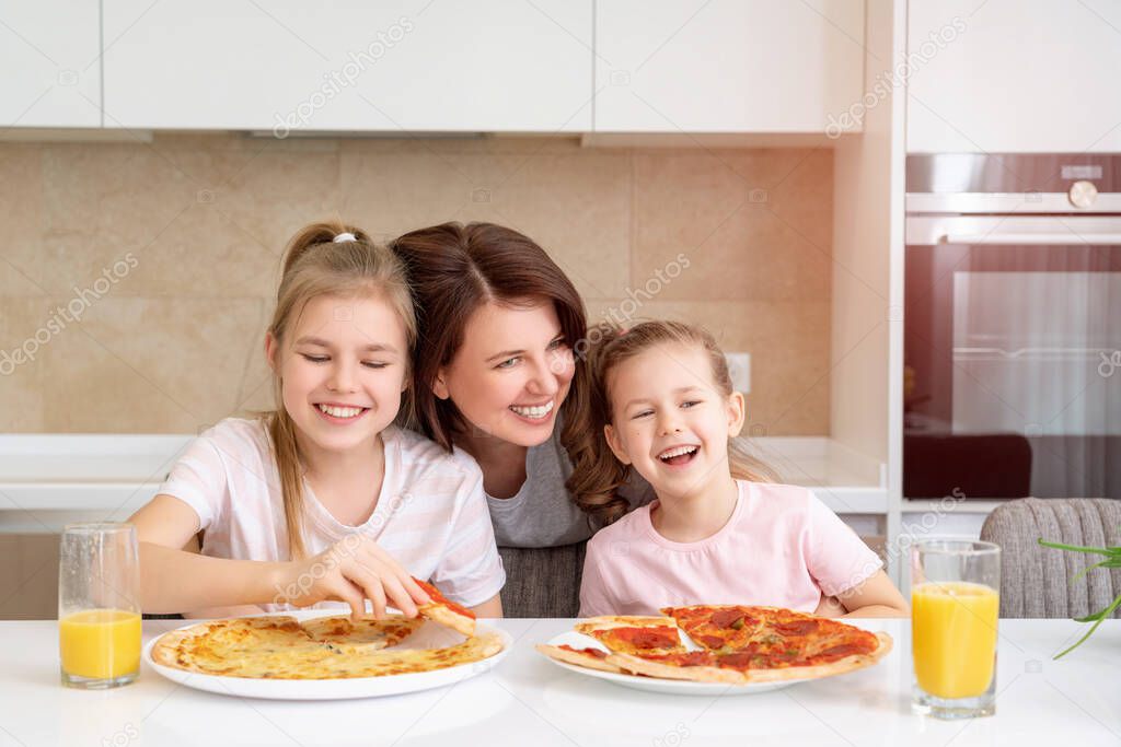 Mother and two daughters eating homemade pizza at a table in kitchen, happy family concept