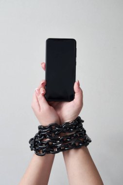 El ve akıllı telefonu sosyal medya ve internet bağımlılığı kavramına bağlayan demir zincir gri arka planda