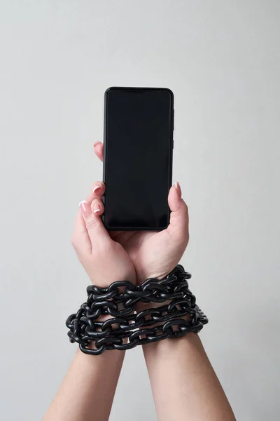 灰色の背景にソーシャルメディアとインターネット中毒の概念で手とスマートフォンを結びつける鉄の鎖 — ストック写真