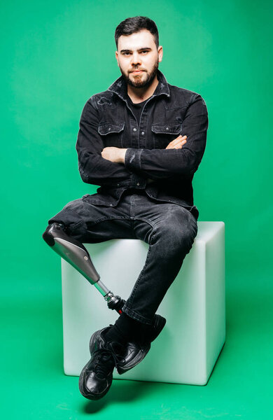 Молодой инвалид с протезной ногой, концепция искусственных конечностей на зеленом фоне
