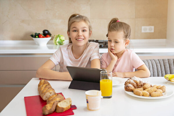 Two sisters having breakfast and watching cartoons on tablet together, happy family concept