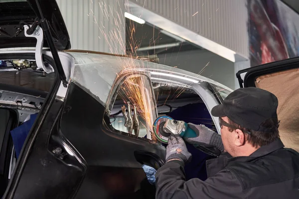 A szervizmunkás megjavítja a sérült autót. A fémtest rögzítésére szolgáló sarokcsiszolóval végzett munka. — Stock Fotó