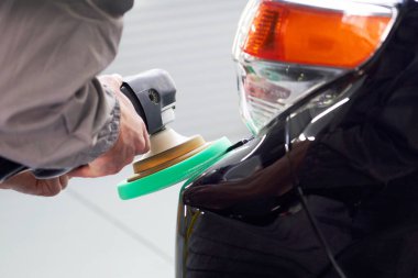 Adam atölyede siyah araba parlatmak için cilalayıcı kullanıyor.