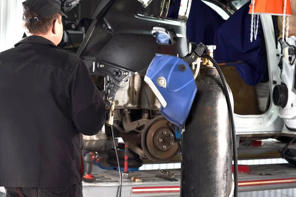 Petugas perbaikan memperbaiki mobil yang rusak. Bekerja dengan penggiling sudut untuk memperbaiki tubuh logam. — Stok Foto