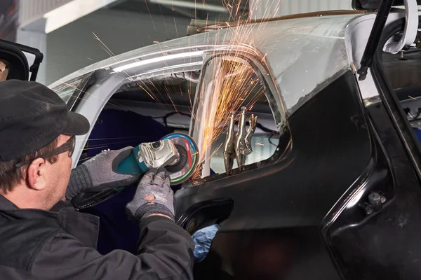 Pracownik serwisu naprawczego naprawia uszkodzony samochód. Praca z szlifierką kątową do mocowania metalowego korpusu. — Zdjęcie stockowe