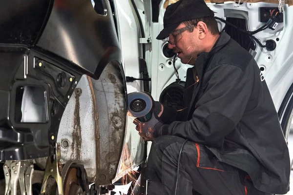 A szervizmunkás megjavítja a sérült autót. A fémtest rögzítésére szolgáló sarokcsiszolóval végzett munka. — Stock Fotó