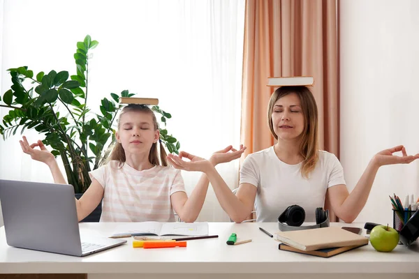 Anne ve kızı evde uzaktan öğrenim sırasında eğleniyorlar, yoga pozisyonunda oturuyorlar, kafalarında kitaplarla, izolasyon konseptiyle. — Stok fotoğraf