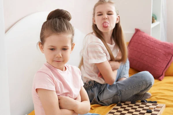 Two sisters playing checkers on a bad and having small fight — Stock Photo, Image