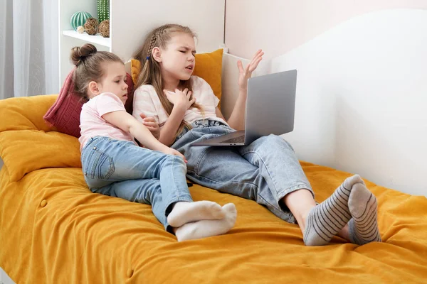 İki kız kardeş aynı yatakta dizüstü bilgisayar kullanarak bir şeyler izliyorlar. — Stok fotoğraf