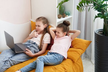 Evde dizüstü bilgisayar kullanan iki kız kardeş.