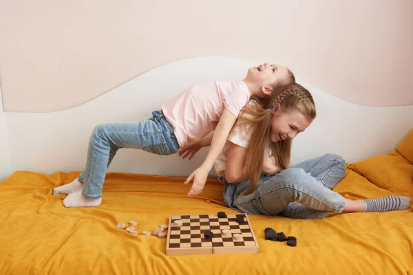 Two sisters playing checkers on a bad having fun at home, happy children concept — Stock Photo, Image