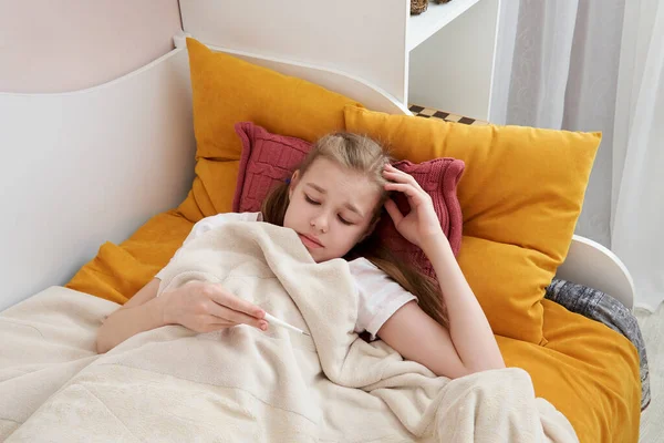 Sick teenage girl laying in bed and looking at a thermometer — Stock Photo, Image