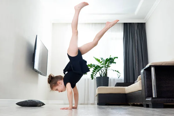 Маленькая девочка занимается гимнастикой дома стоя на руках вверх ногами — стоковое фото