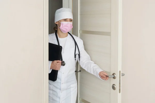 Врач в медицинской маске со стетоскопом открывает дверь в комнату — стоковое фото