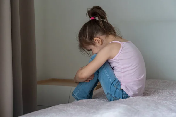 Una niña triste sentada en una cama, vista trasera —  Fotos de Stock