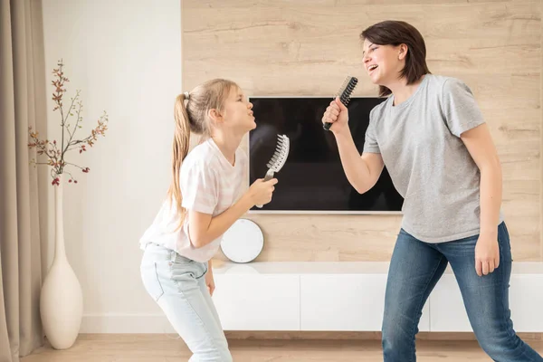 Happy family young adult mother and cute teen daughter having fun singing karaoke song in hairbrushes. mother laughing enjoying funny lifestyle activity with teenage girl at home together. — Stock Photo, Image