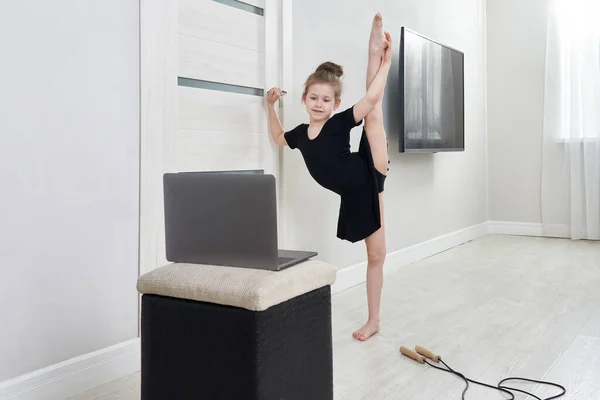 Bambina che fa esercizi di ginnastica a casa utilizzando l'apprendimento online con computer portatile, concetto di educazione a Internet — Foto Stock