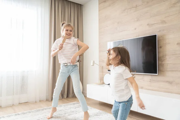 Zwei Schwestern haben Spaß beim Tanzen im Wohnzimmer und singen Karaoke, glückliches Familienkonzept — Stockfoto