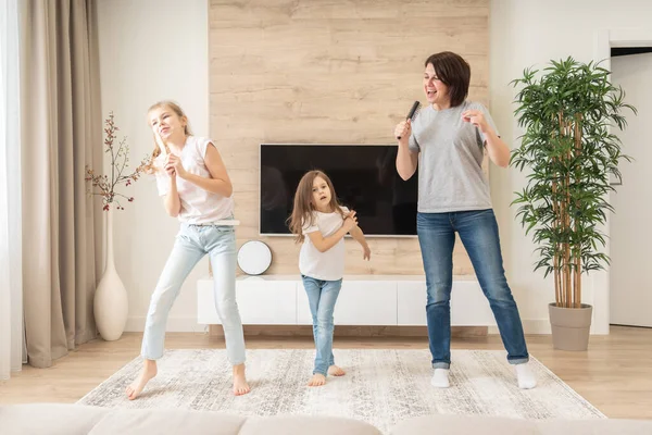 Glückliche Mutter und zwei Töchter, die Spaß daran haben, Karaoke-Lieder in Haarbürsten zu singen. Mutter lacht und genießt lustige Lifestyleaktivitäten mit Teenager-Mädchen zu Hause zusammen. — Stockfoto