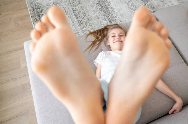 Preteen ragazza sdraiata sul divano con i piedi nudi alzando alto — Foto Stock