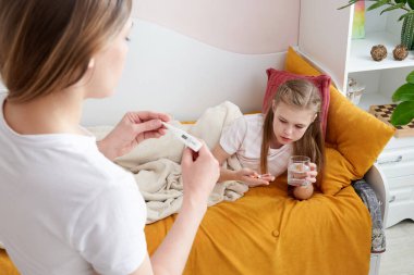 Anne hasta çocuğuna ilaç ve bir bardak su veriyor. Annem hasta kızımdan hap içmesini istedi.