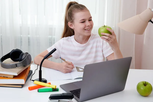 Yeşil elma tutan genç kız evde dizüstü bilgisayarla ders çalışıyor. — Stok fotoğraf