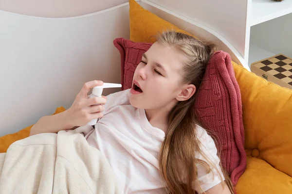 Evdeki yatakta sprey kullanan, boğaz ağrısı çeken bir kız. — Stok fotoğraf