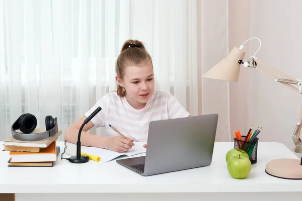 İnternette kulaklık ve dizüstü bilgisayarla öğrenen genç bir kızın portresi. Evdeki masasında oturmuş ödev yaparken not alıyor. — Stok fotoğraf