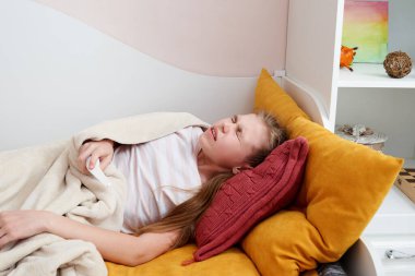 Evdeki yatakta sprey kullanan, boğaz ağrısı çeken bir kız.