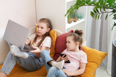 Evde dizüstü bilgisayar kullanan iki kız kardeş.