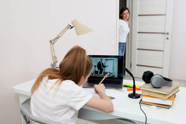 Madre viendo a su hija haciendo la tarea en el ordenador portátil en casa — Foto de Stock