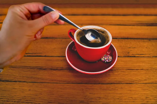 hand stirs a cup of coffee with a teaspoon