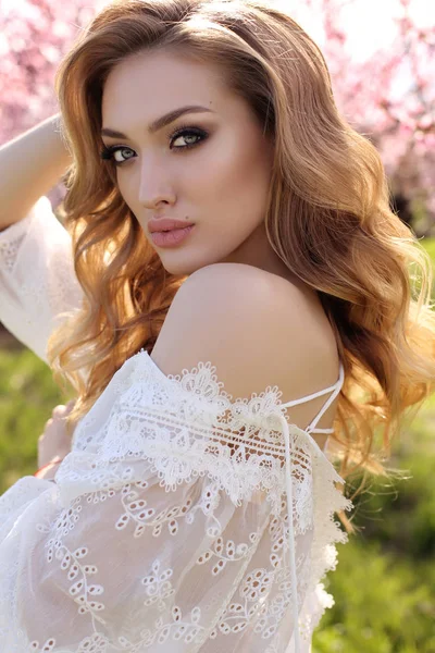 Magnifique jeune femme en robe élégante posant dans le jardin avec des fleurs — Photo
