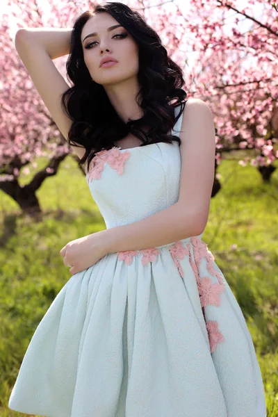 Prachtige jonge vrouw in elegante jurk poseren in de tuin met perzik bloesem bomen — Stockfoto