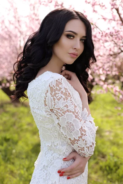 Женщина с темными волосами в элегантном платье позирует в цветущем саду — стоковое фото