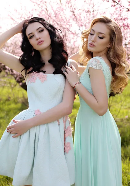 Mooie vrouwen in elegante jurken poseren in bloesem tuin — Stockfoto
