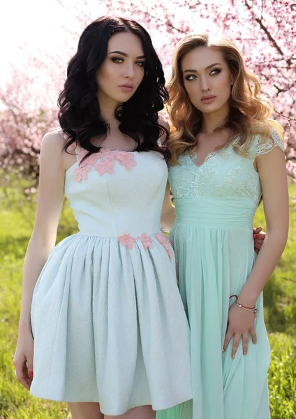 Hermosas mujeres en vestidos elegantes posando en el jardín de flores —  Fotos de Stock