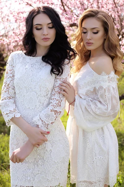 Schöne Frauen in eleganten Kleidern posieren im blühenden Garten — Stockfoto
