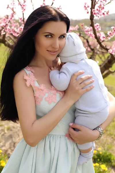 Kvinna i elegant klänning poserar med sin baby pojke i blossom garde — Stockfoto