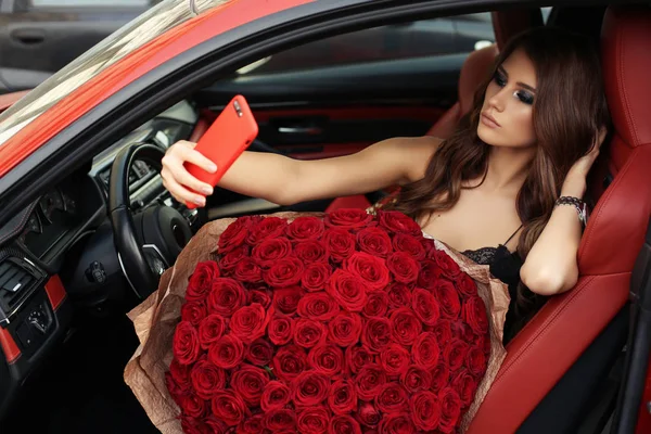 Beautiful girl  in elegant dress posing in luxurious car with bo — Stock Photo, Image