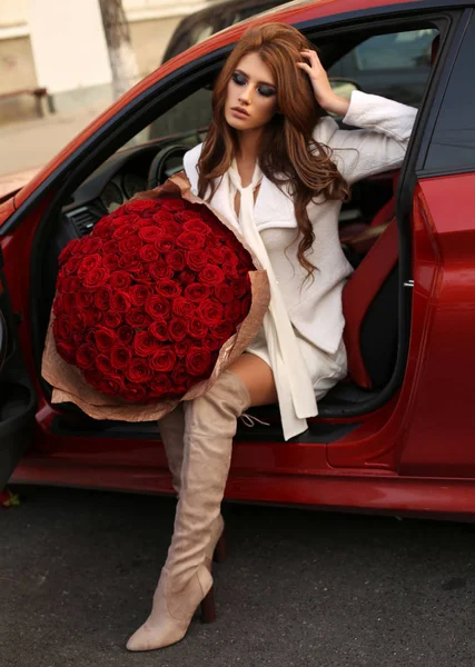 Beautiful girl  in elegant dress posing in luxurious car with bo — Stock Photo, Image