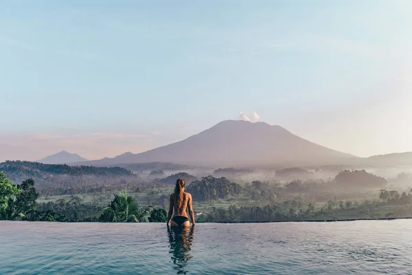 Schönes Mädchen in der Nähe von Schwimmbad mit fantastischem Vulkan — Stockfoto