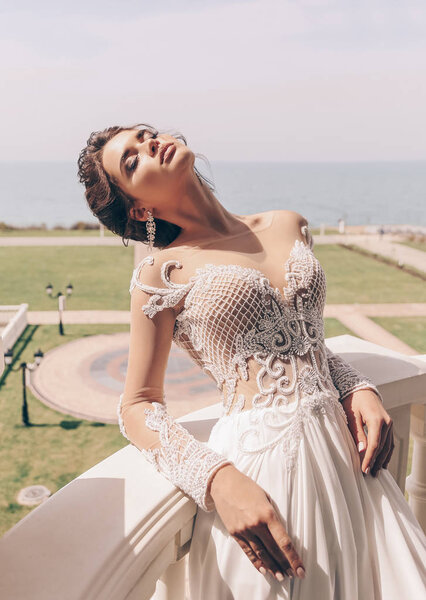 fashion photo of beautiful woman with dark hair in luxurious wedding dress posing outdoor