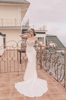 lüks düğün elbise ve aksesuarlar açık deniz ve dağ manzaralı, poz sarışın saçlı güzel kadın moda fotoğrafı